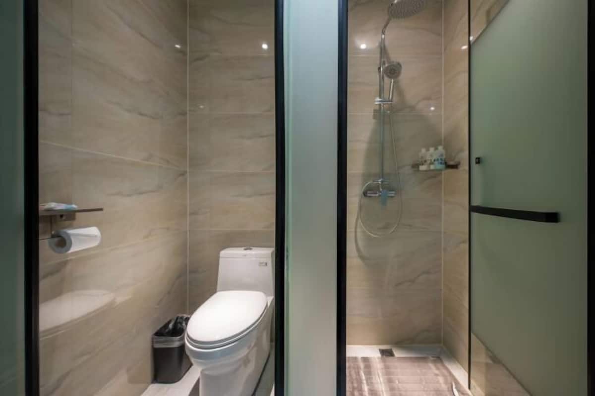 Une salle de bain moderne avec une douche à parois de verre, des toilettes et un rouleau de papier toilette posé sur une étagère.