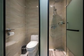 Une salle de bain moderne avec une douche à parois de verre, des toilettes et un rouleau de papier toilette posé sur une étagère.