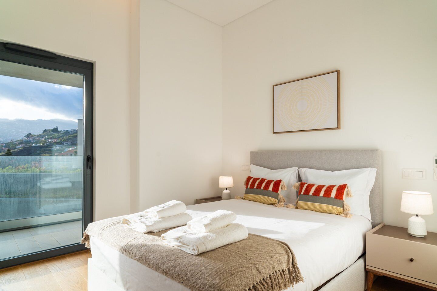 A hotel room with a bed, two bedside tables, a window with a view, and a framed picture on the wall.