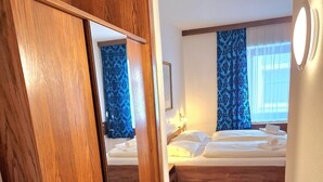 A hotel room with a wooden floor, a bed with white linens, a nightstand, and a window with blue curtains. - Zum Goldenen Kreuz (Eferding)