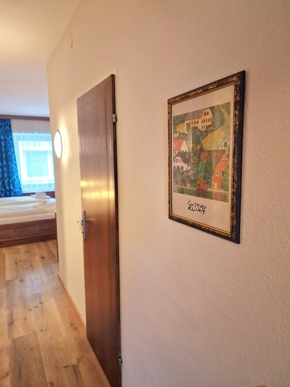 A hallway with a wooden door, a framed picture on the wall, and a bed in the background. - Zum Goldenen Kreuz (Eferding)