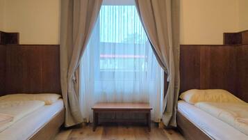 Una habitación con dos camas individuales, un banco y una ventana con cortinas.