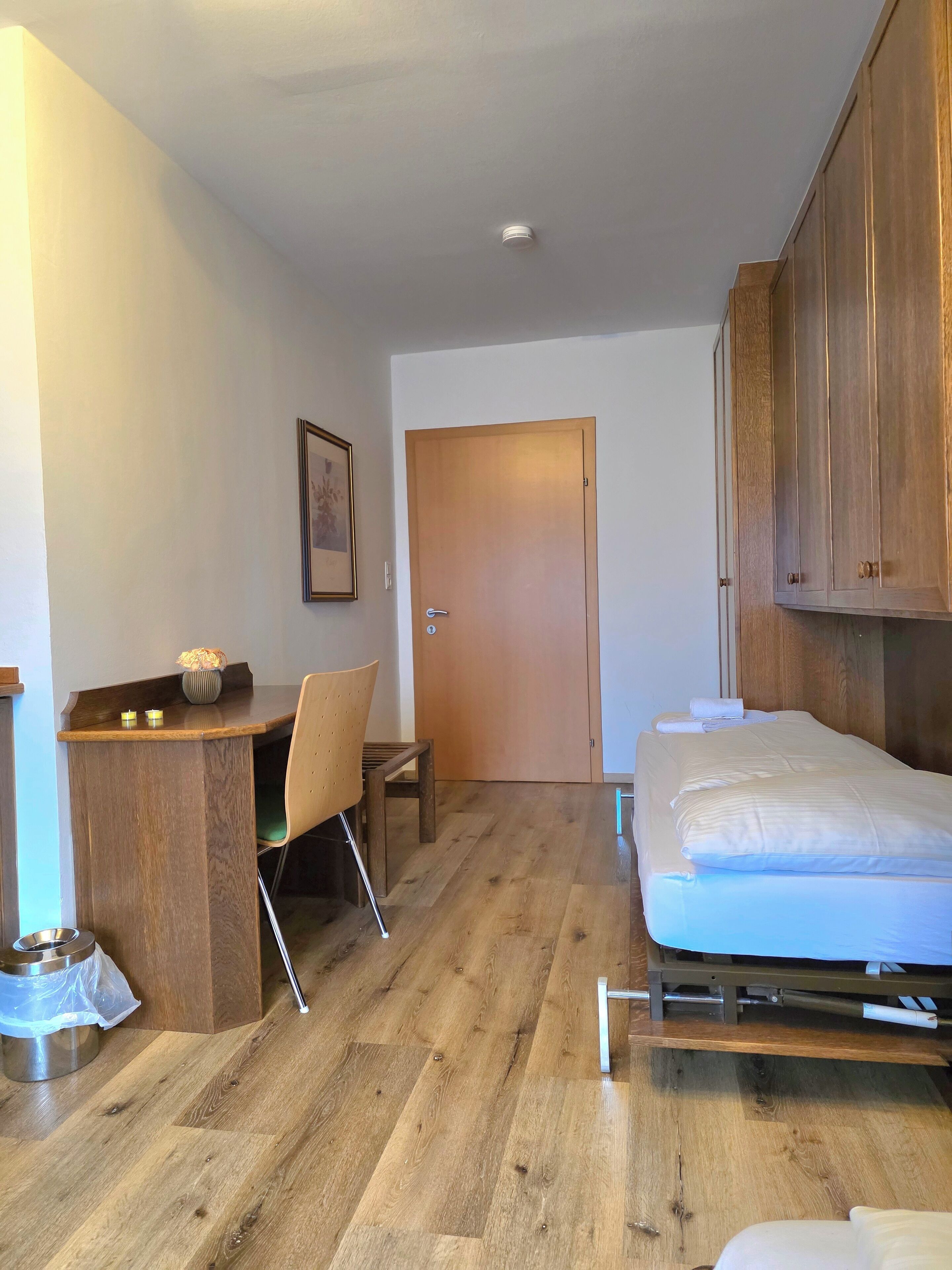 Une petite pièce avec un bureau en bois, un lit et une porte.