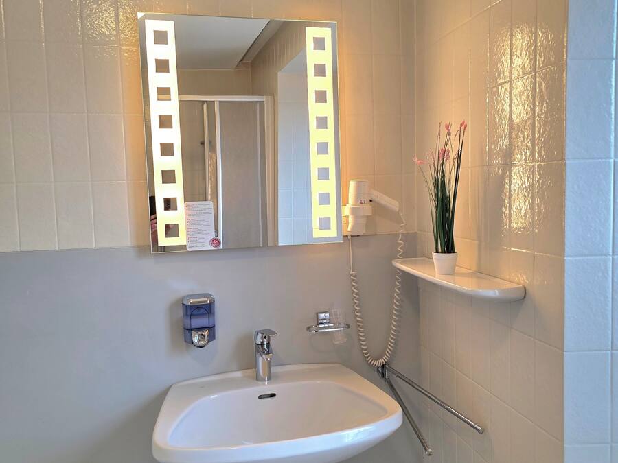 Un baño con lavamanos blanco, un espejo con iluminación, toallero y radiador.