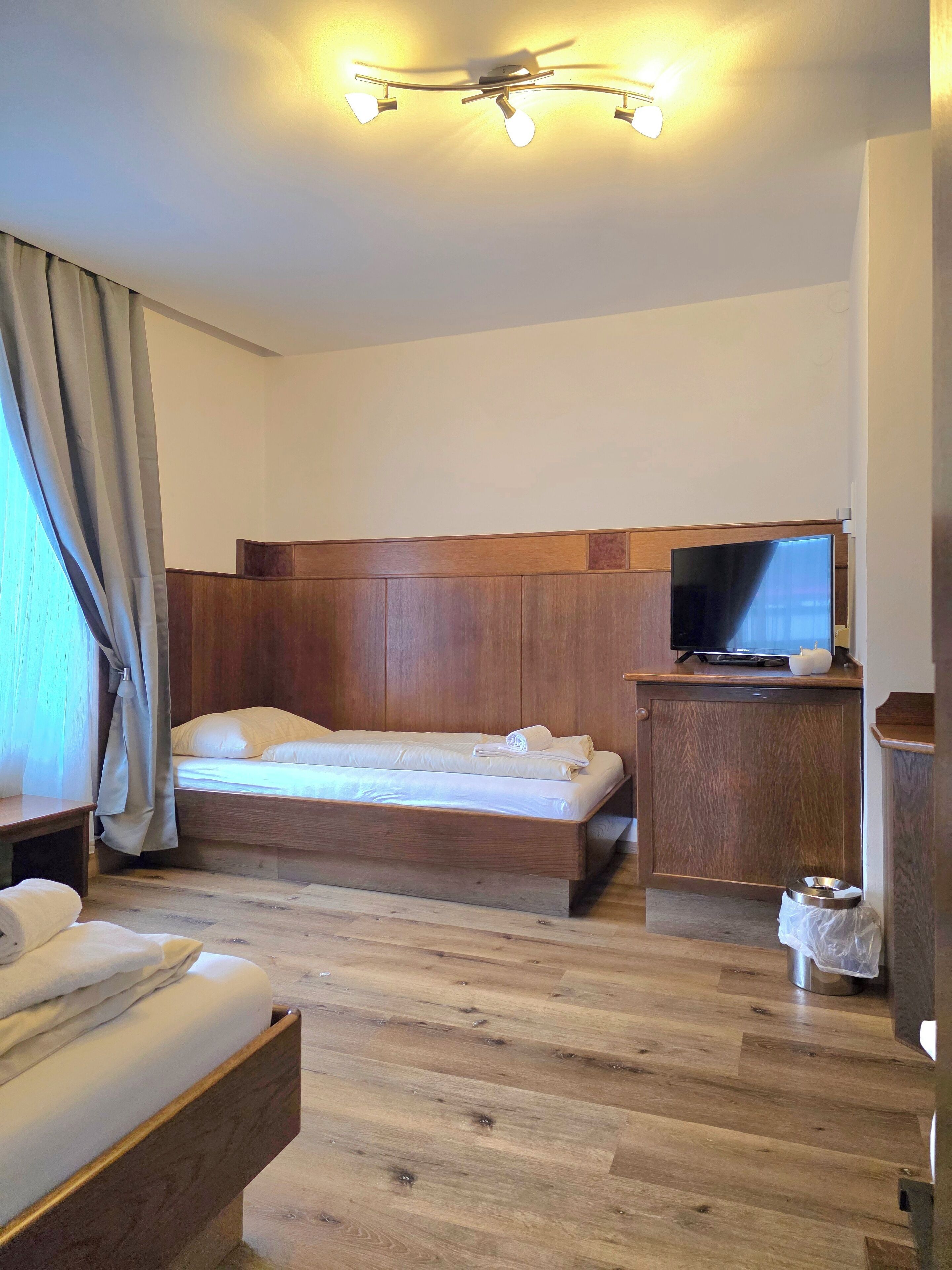 A hotel room with a wooden bed, a television on a wooden cabinet, and a ceiling light fixture.