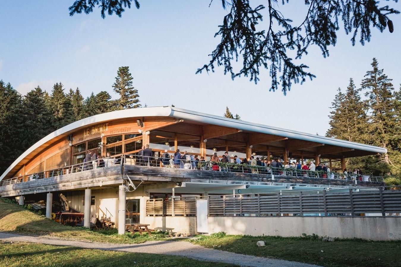 A restaurant with an outdoor seating area, a covered deck, and a view of the surrounding forest.