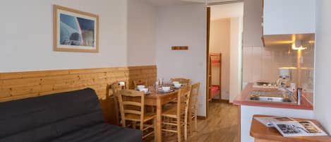 A cozy room with a wooden bench, a dining table with chairs, a bunk bed, and a kitchenette.