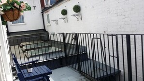 Een balkon met een zwart metalen hekwerk, een blauwe tafel en een hangmand met bloemen.