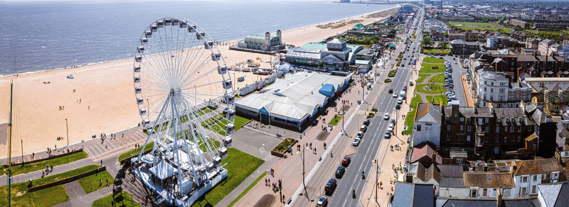 Un paysage urbain côtier avec une grande grande roue, une plage et un mélange de bâtiments modernes et historiques.