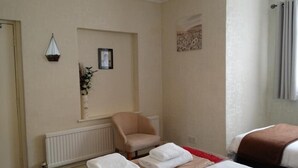 A hotel room with a bed, a chair, a radiator, a framed picture, and a window with curtains. - The Beach House (Great Yarmouth)