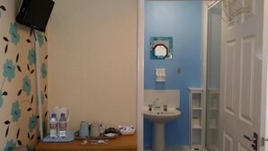 Een badkamer met een wastafel, spiegel en een klein plankje. Er staat een houten dressoir met toiletartikelen en een blauwe mat op de vloer.