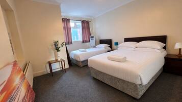 A hotel room with two beds, a small table, a lamp, and a window with curtains.