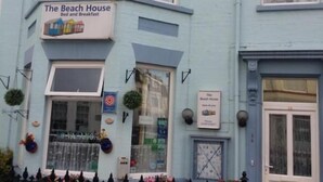 Een lichtblauw gebouw met een bord waarop staat: The Beach House Bed and Breakfast.