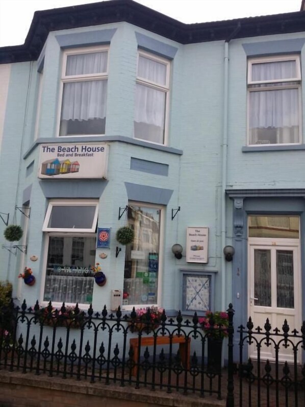 Een lichtblauw gebouw met een bord waarop staat: The Beach House Bed and Breakfast.
