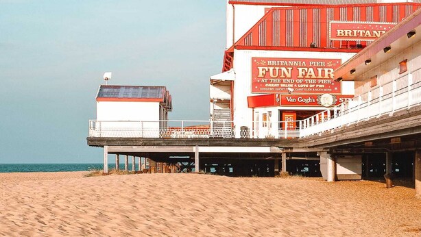 Een steiger met een bord 'Britannia Pier', een klokkentoren en een gebouw met een rood-witte gevel.