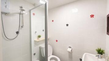 A bathroom with a glass-enclosed shower, a toilet, and a sink with a small plant.