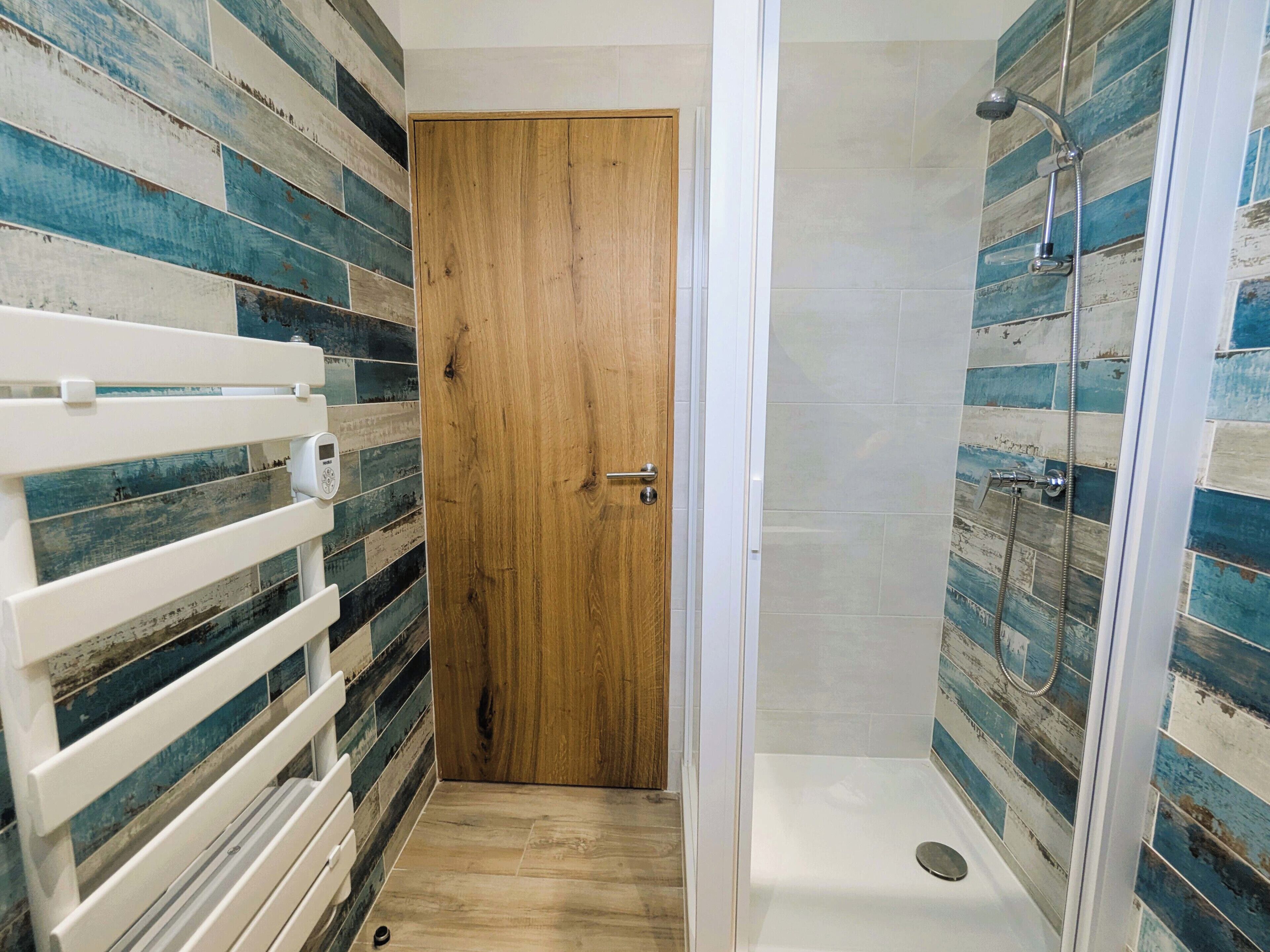 A bathroom with a wooden door, a shower with a glass enclosure, and a white bench.