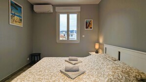 A bedroom with a large bed, a window with a view, and a nightstand with a lamp. - Penthouse with large terrace, near beaches (Toulon)