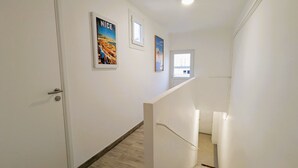 A clean, white hallway with wooden flooring, a white door, and a staircase with a white railing. There are three framed pictures on the wall. - Penthouse with large terrace, near beaches (Toulon)