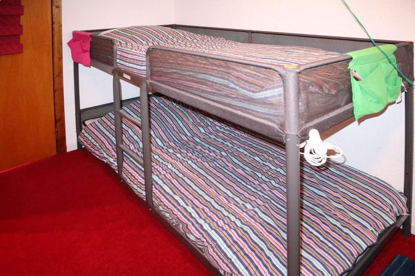 A bunk bed with striped bedding and a red carpeted floor.
