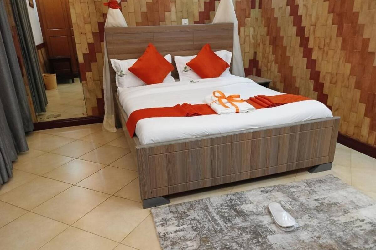 A neatly made bed with white and orange bedding, a wooden headboard, and a grey patterned rug on the floor.