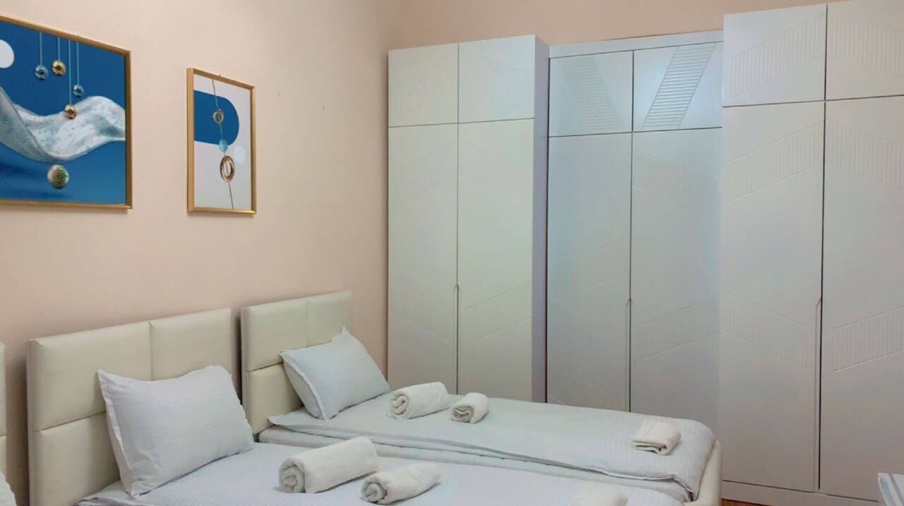A hotel room with two beds, a large wardrobe, and two framed artworks on the wall.