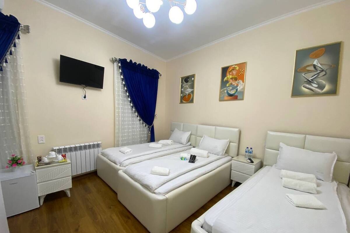 A hotel room with two beds, a TV, a radiator, and artwork on the walls.