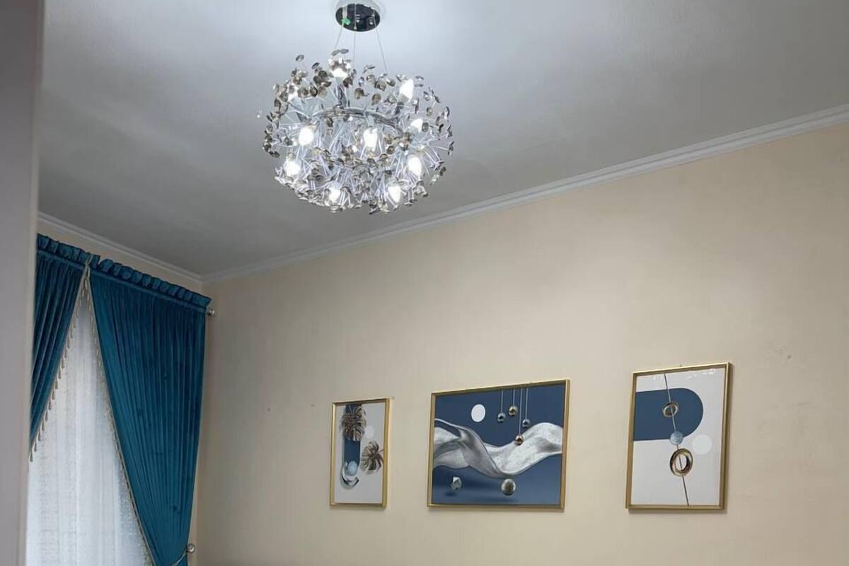 A hotel room with two beds, a chandelier, and three framed artworks on the wall.