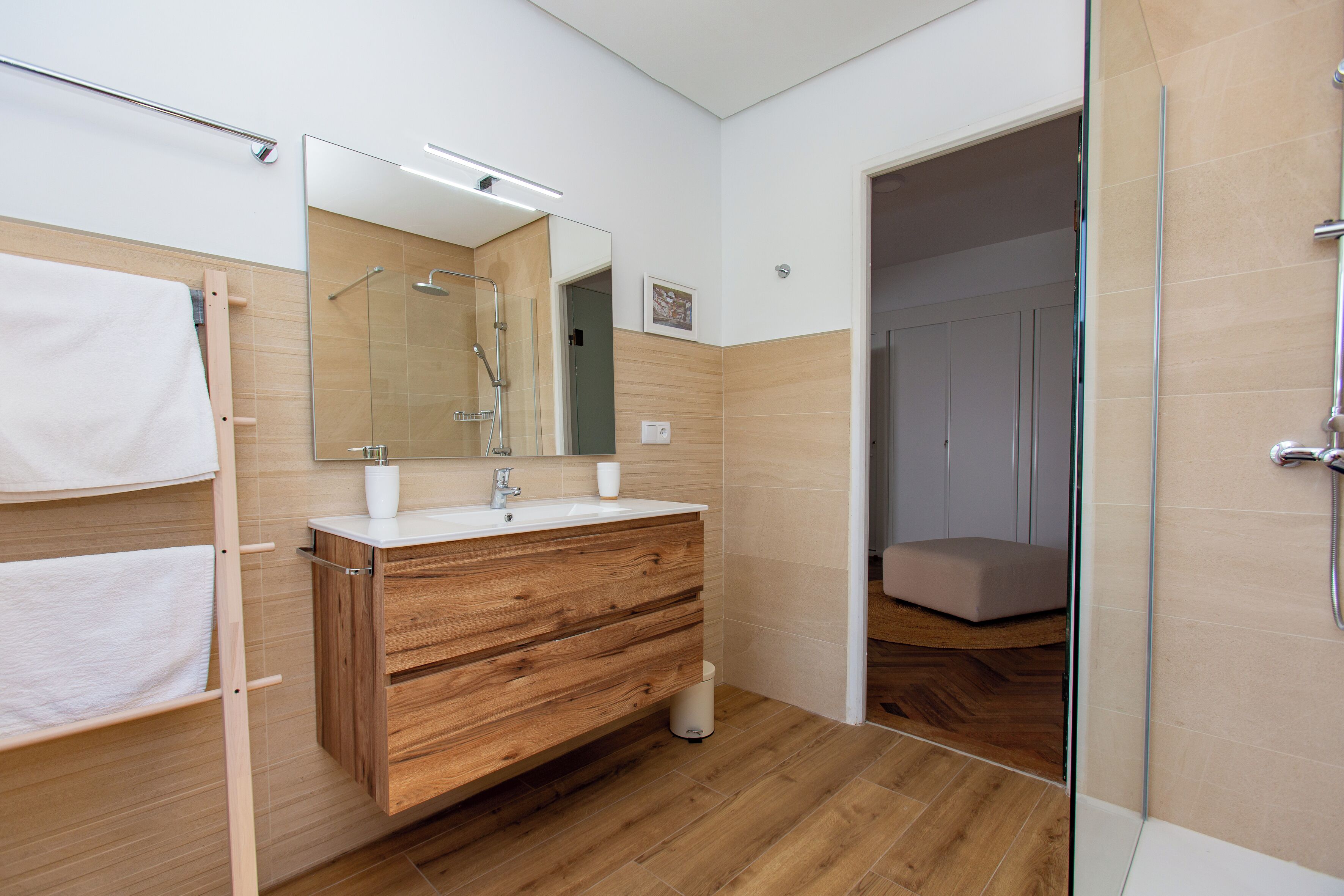 A modern bathroom with a wooden vanity, a glass shower enclosure, and a walk-in closet.
