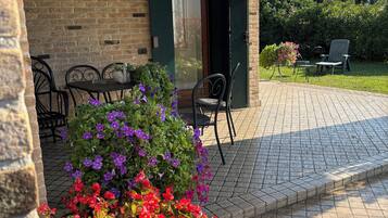 A brick building with a patio area featuring a table and chairs, surrounded by potted plants with red and purple flowers.