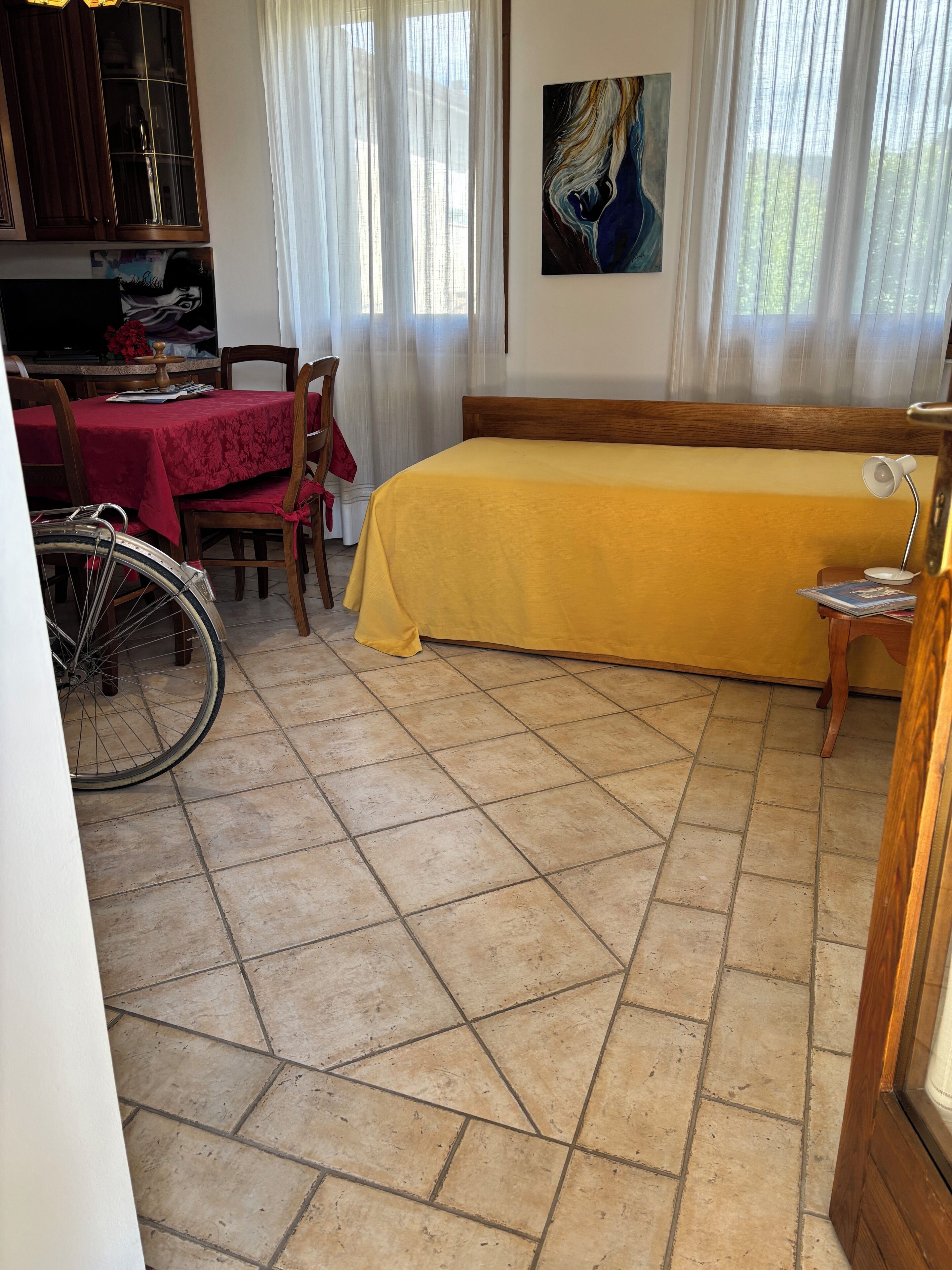 Een kamer met een bed, een eettafel met stoelen, een fiets en een schilderij aan de muur.