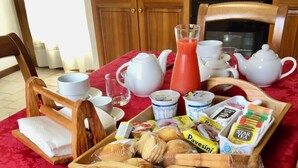 A breakfast table with a red tablecloth, wooden chairs, a tray of bread, a pitcher of orange juice, a teapot, cups, and a glass. - B&B Alla Suite (Pieve di Soligo)