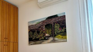 A room with a yellow table, a painting of a bridge, an air conditioning unit, and a wooden wardrobe. - B&B Alla Suite (Pieve di Soligo)