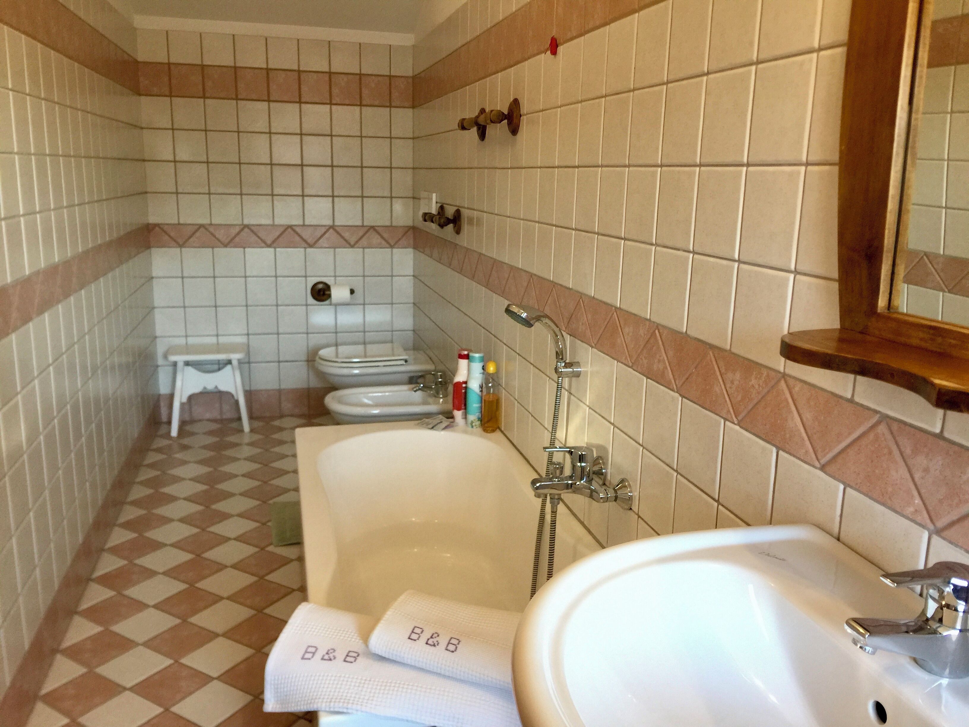A bathroom with a large bathtub, two toilets, a small bench, and a mirror above the sink.