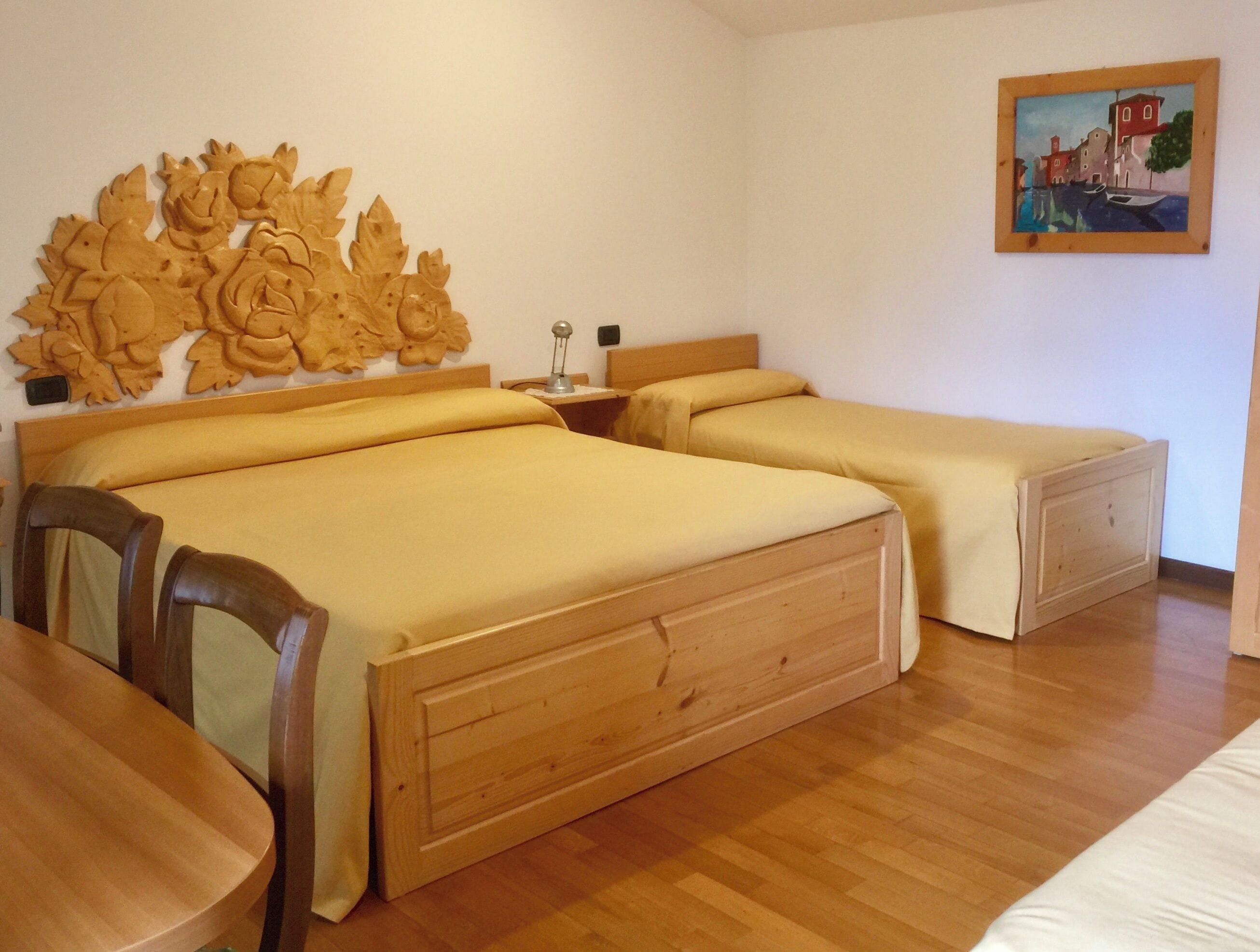 Una habitación de hotel con dos camas de madera, un cabecero de madera, una mesa de madera y un cuadro en la pared.