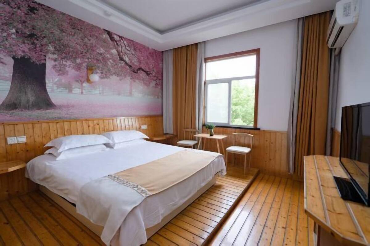 A bedroom with a large bed, wooden flooring, a mural on the wall, a window with curtains, and a TV on a wooden table.