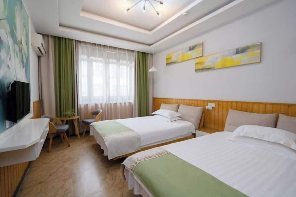 A hotel room with two beds, a desk, a chair, and a TV.