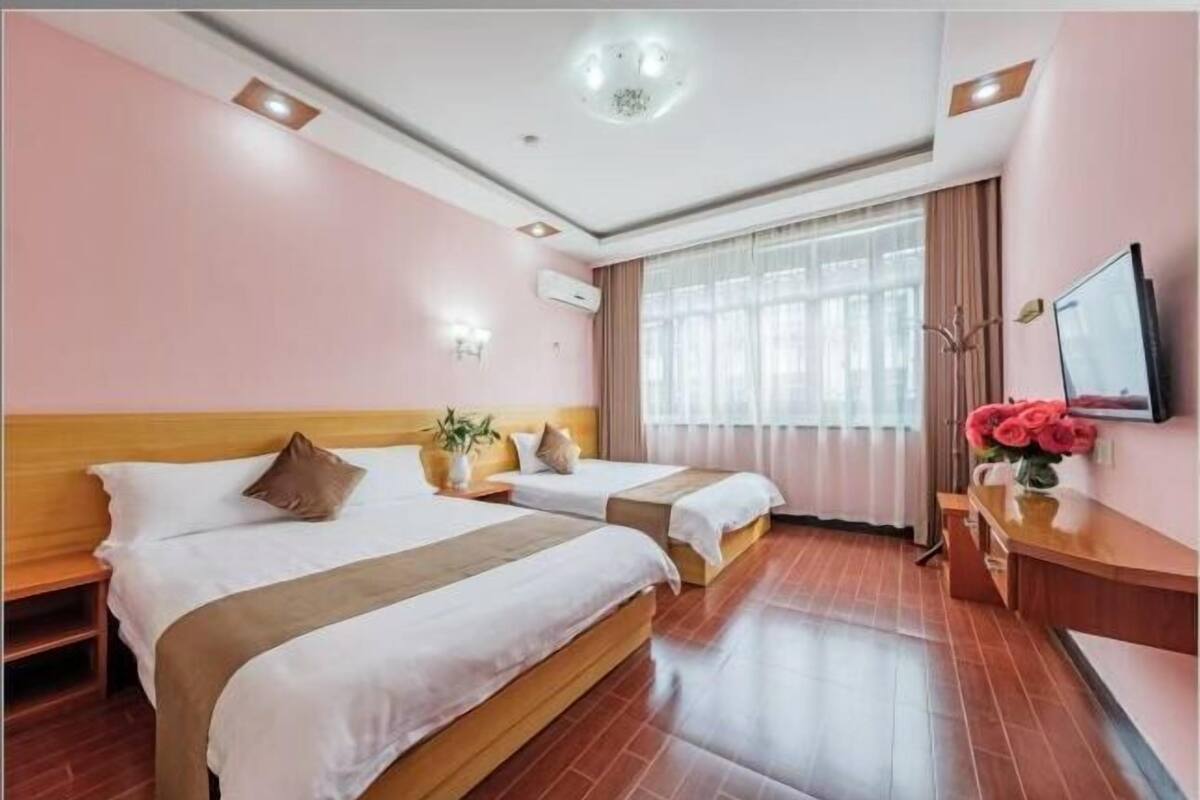 A hotel room with two beds, a wooden headboard, a flat-screen TV, a bedside table, a mirror, and a window with curtains.
