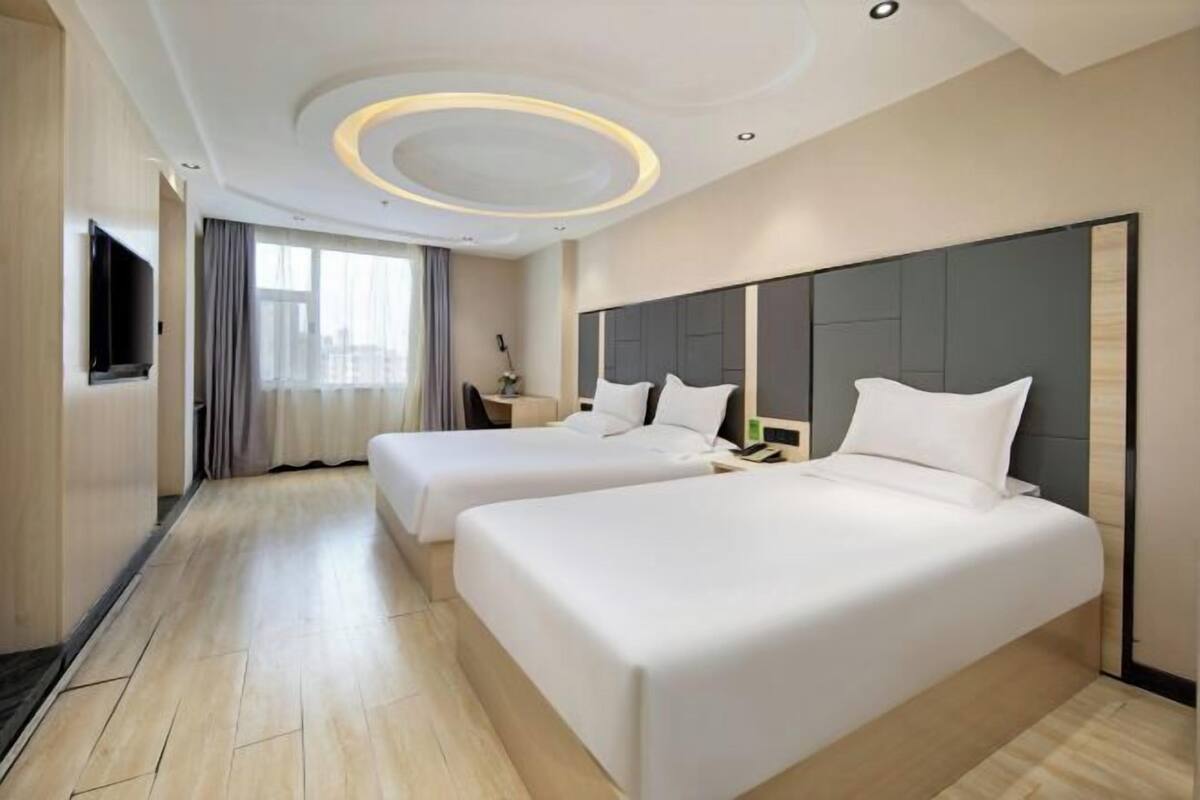 Habitación de hotel con dos camas, un televisor de pantalla plana, un ventanal grande con cortinas y un diseño moderno de techo.