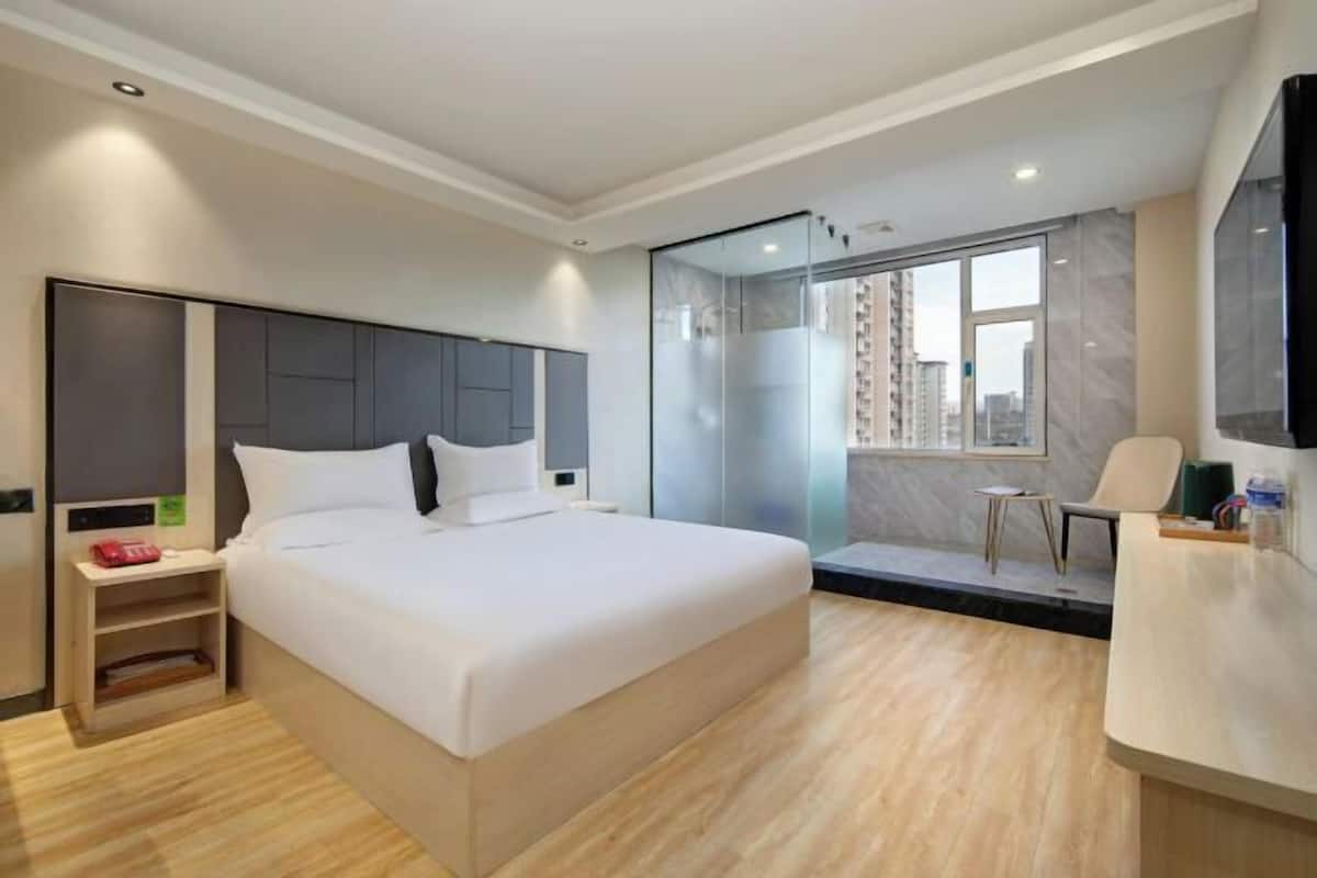 Una habitación de hotel moderna con una cama grande, un escritorio, una silla y un box de ducha de vidrio.