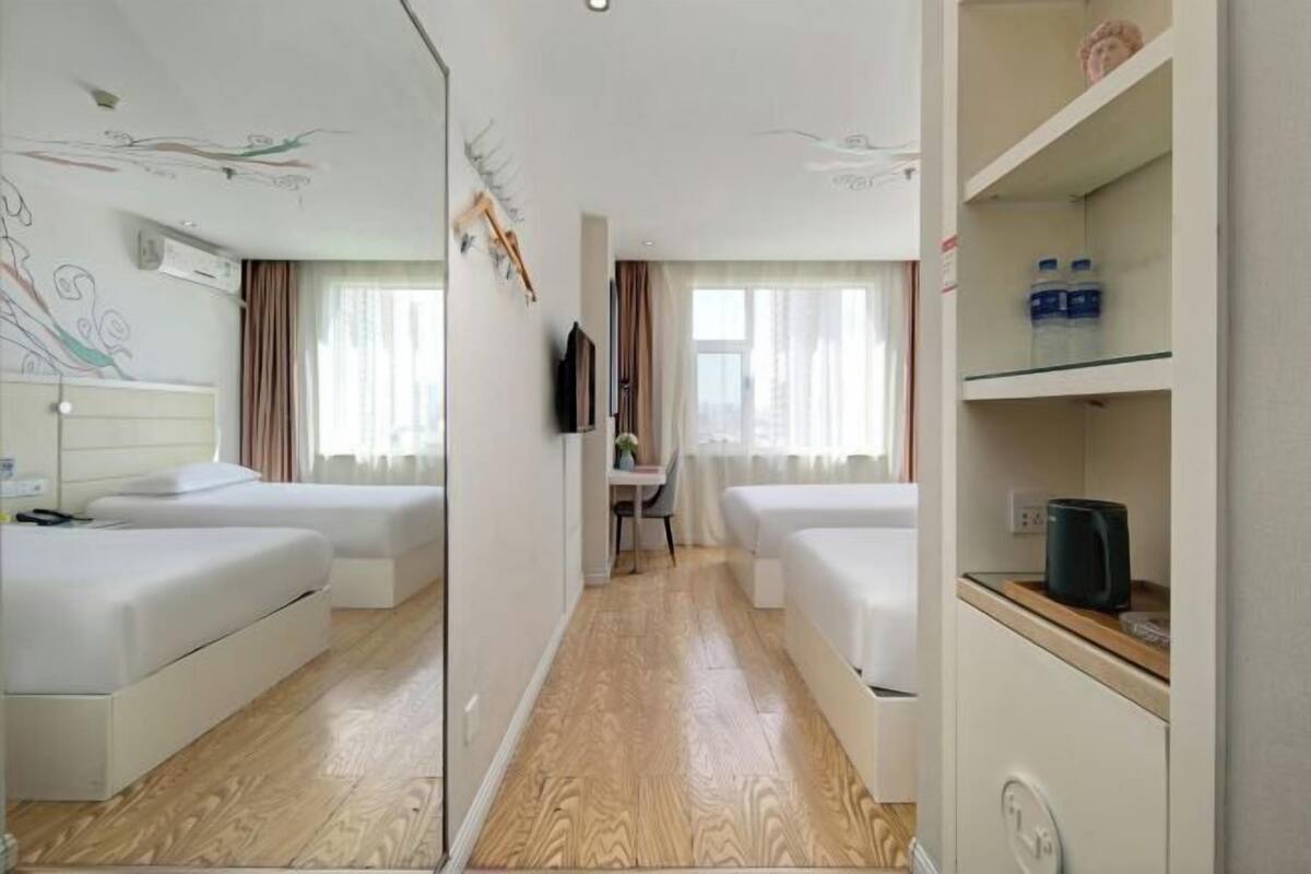 Habitación de hotel con dos camas, un escritorio, un espejo y una estantería con botellas de agua.