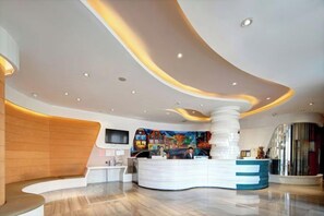 A modern hotel lobby with a curved reception desk, a large abstract painting, and a seating area.