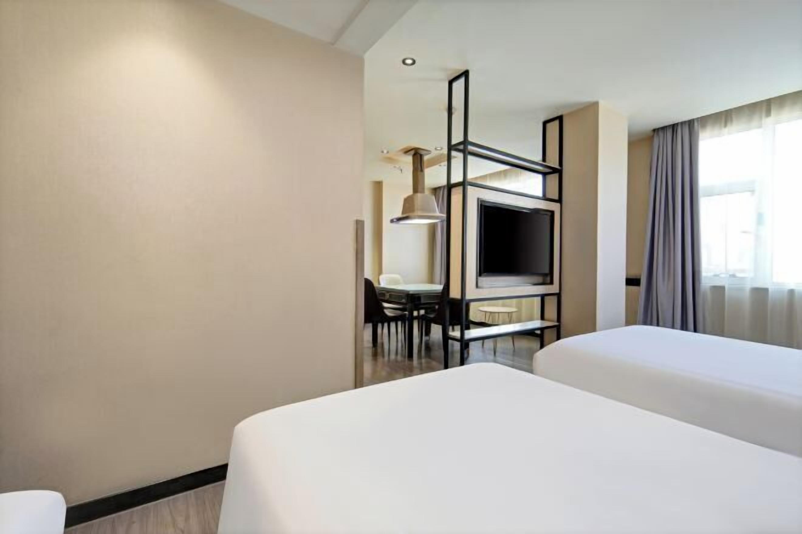 A hotel room with two beds, a TV, a desk with a chair, and a window with curtains.