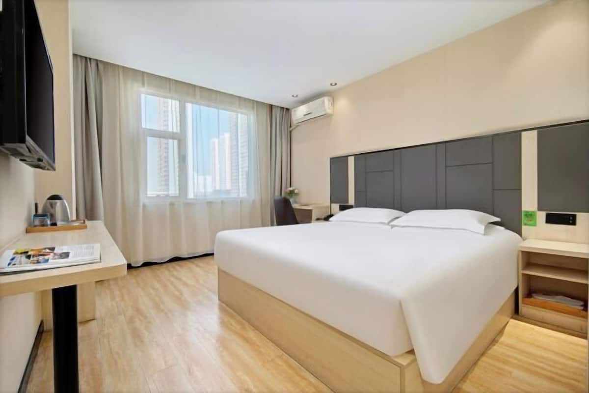 Una habitación de hotel moderna con una cama grande, un escritorio con silla, un televisor de pantalla plana y un ventanal con cortinas.