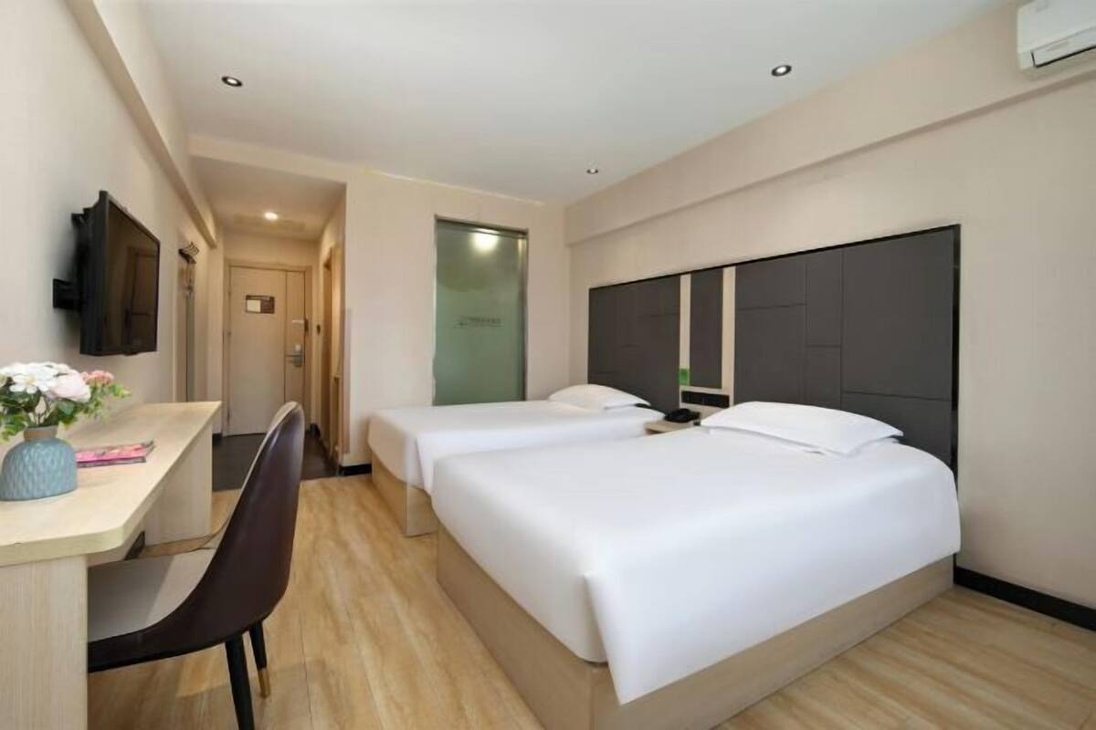 Habitación de hotel con dos camas, un escritorio, una silla y un televisor.