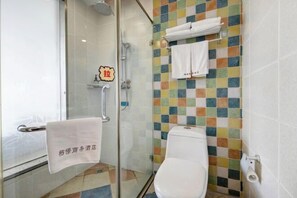 Ein Badezimmer mit Duschkabine aus Glas, Toilette und einer gefliesten Wand mit farbigem Muster.