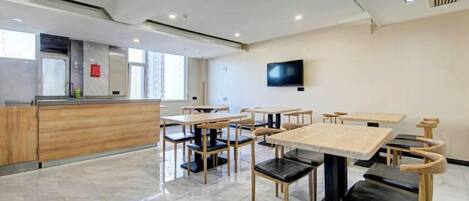 Een moderne eetruimte met meerdere tafels en stoelen, een keukenblad en een flatscreen televisie aan de muur.