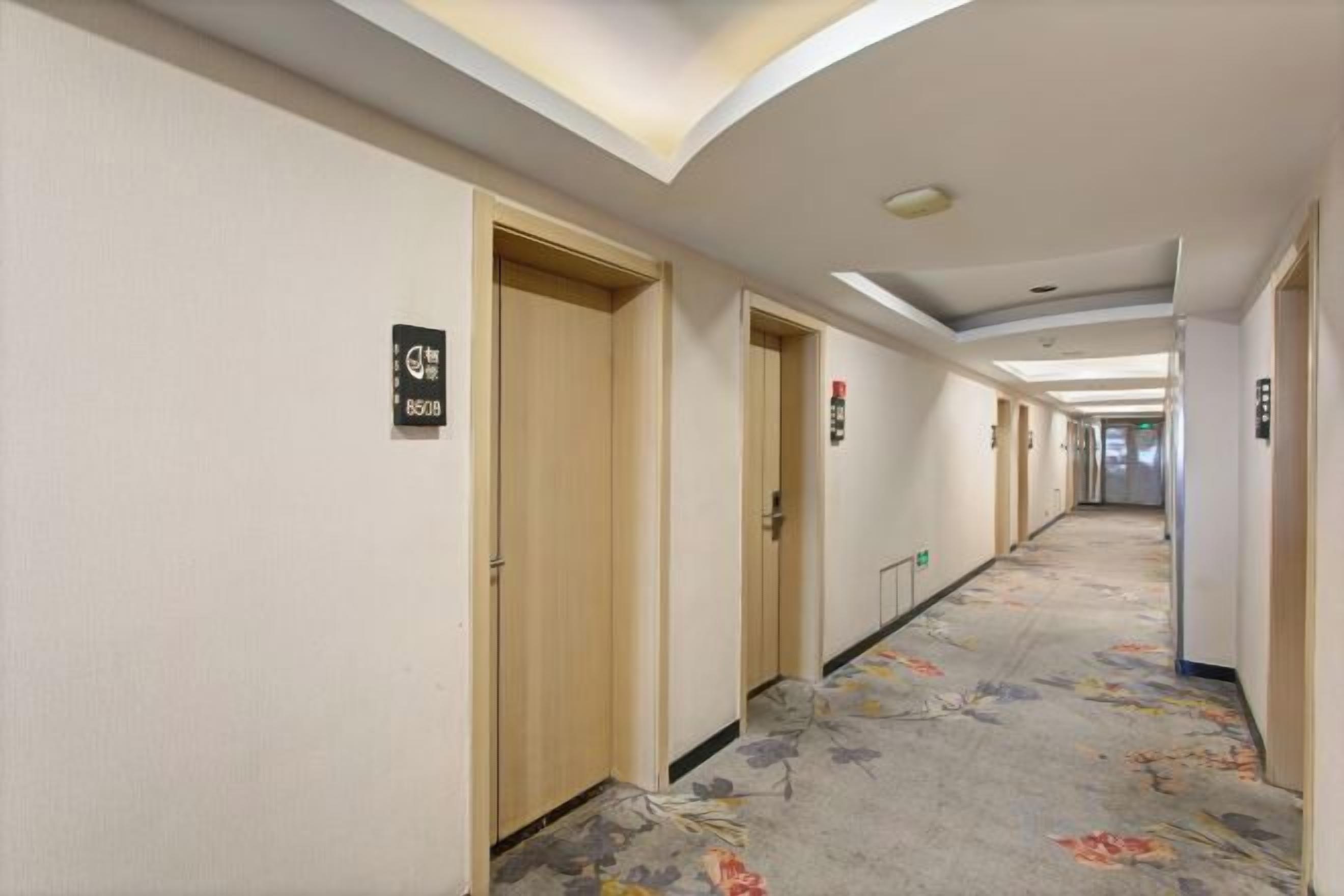 A hotel corridor with doors, carpeted flooring, and ceiling lights.