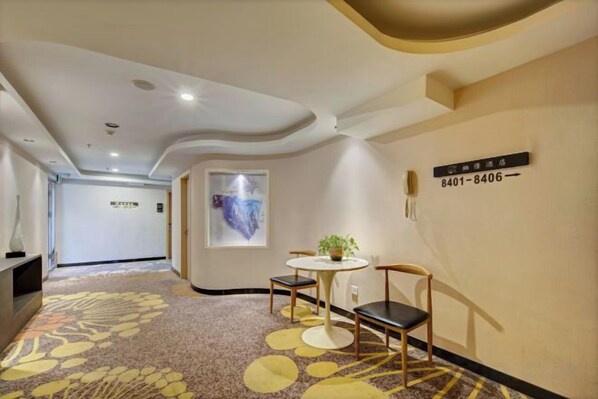 A hotel corridor with a carpeted floor, a round table with chairs, a potted plant, and a wall-mounted sign with room numbers. - New Tangji Hotel (Taiyuan South Neihuan Street Jianshe South Road) (Taiyuan)