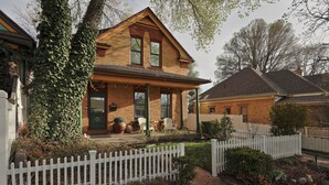 Een huis met twee verdiepingen, een voortuin met een witte picket fence en een bakstenen gevel.